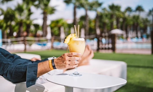 Persona sosteniendo un c&oacute;ctel tropical junto a una piscina.
