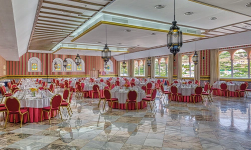 Sal&oacute;n de banquetes con mesas redondas y sillas rojas, decorado con l&aacute;mparas.