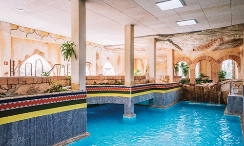 Piscina interior con decoraci&oacute;n tem&aacute;tica y un puente cruzando el agua azul.