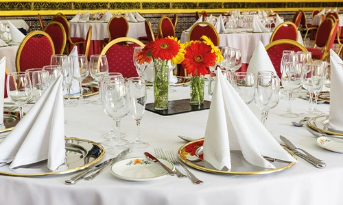 Mesa elegante con copas, platos y servilletas, adornada con flores rojas.