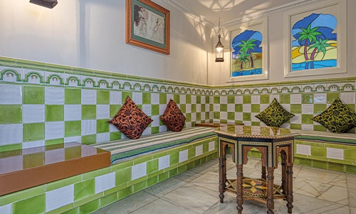 Sala con banco de azulejos verdes y mesa decorativa, l&aacute;mpara y cojines.