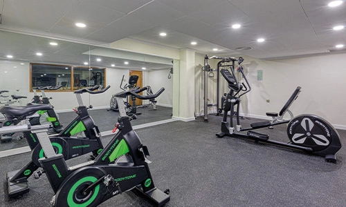 Gimnasio con bicicletas est&aacute;ticas, m&aacute;quina de remo y espejo grande.