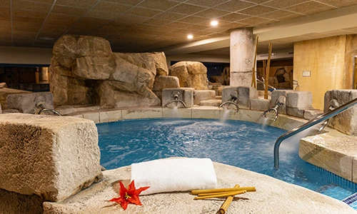 Spa con piscina de hidromasaje rodeada de rocas y toalla con flor roja.