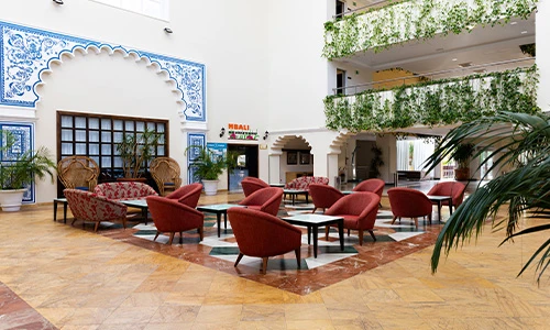 Sala con sillones rojos, plantas y decoraciones de estilo &aacute;rabe en las paredes.