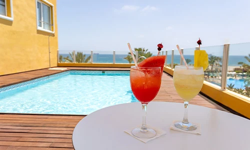 C&oacute;cteles junto a una piscina con vista al mar en un d&iacute;a soleado.