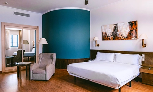 Habitaci&oacute;n de hotel con cama, sill&oacute;n y decoraci&oacute;n moderna en tonos tierra.