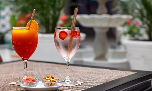 Dos copas con c&oacute;cteles y snacks en una mesa al aire libre.