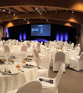 Sal&oacute;n de eventos con mesas, sillas blancas y pantalla de presentaci&oacute;n