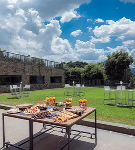 Mesa de buffet al aire libre en jard&iacute;n con cielo nublado y sillas.