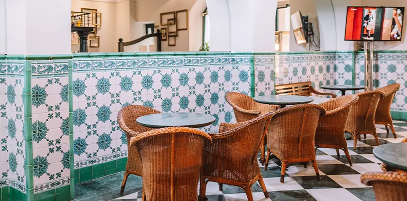 Interior de cafeter&iacute;a con mesas y sillas de mimbre y azulejos decorativos