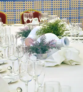 Mesa servida con arreglos de plantas y copas de cristal en un banquete.