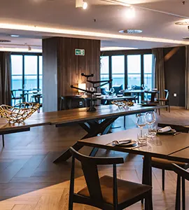 Comedor de hotel moderno con mesas, sillas y gran ventanal con luz natural