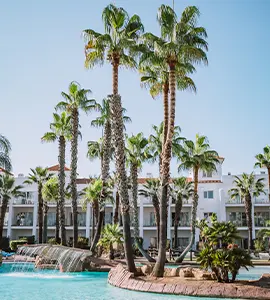 Piscina con palmeras y edificio blanco bajo cielo azul claro