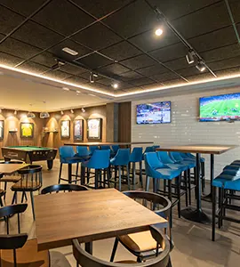 Sala con mesas y sillas azules, televisores y decoraci&oacute;n en pared blanca.