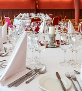 Mesa de banquete con copas y cubiertos en un sal&oacute;n decorado.