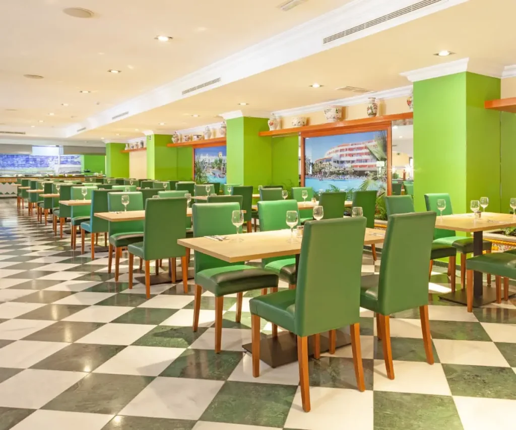 Sala de restaurante con mesas y sillas verdes, vista a piscina y ventanas