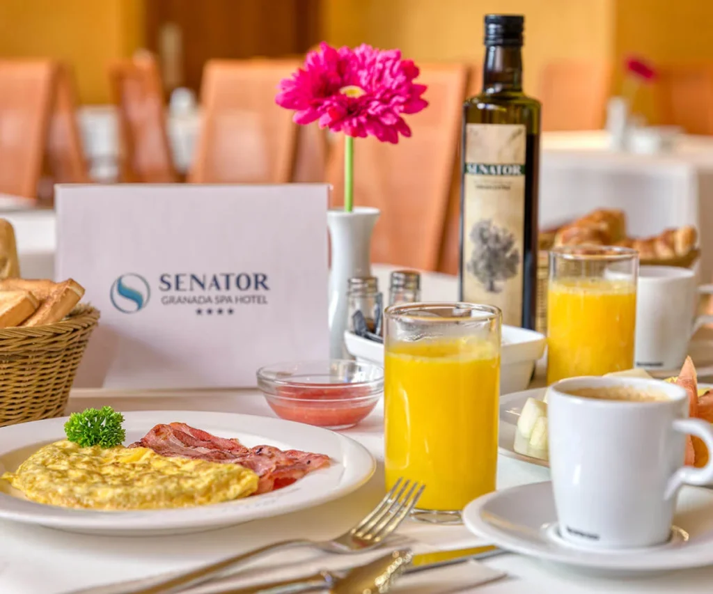 Desayuno en hotel: huevos, tocino, jugo y flor rosa en mesa con botella