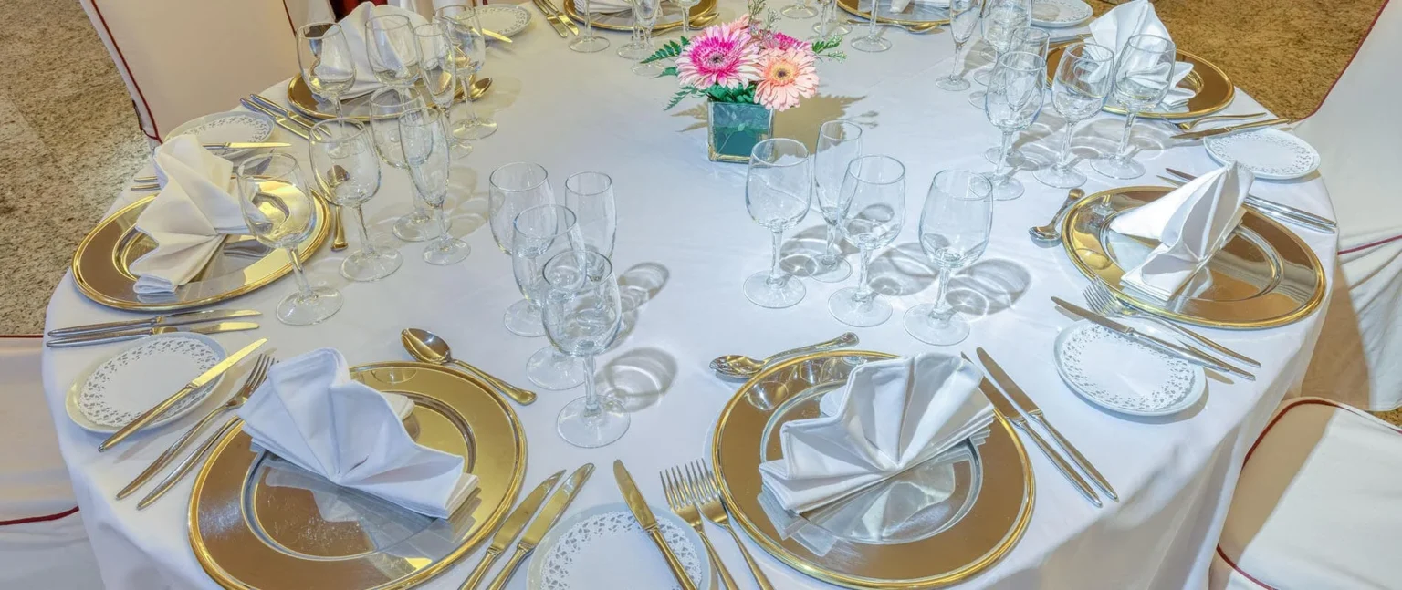 Mesa servida con platos dorados, copas y un ramo de flores.