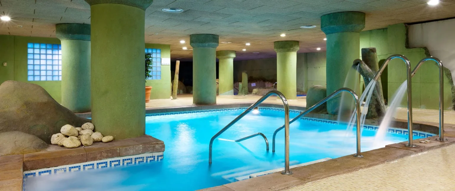 Piscina cubierta con columnas verdes y toboganes de agua en el interior