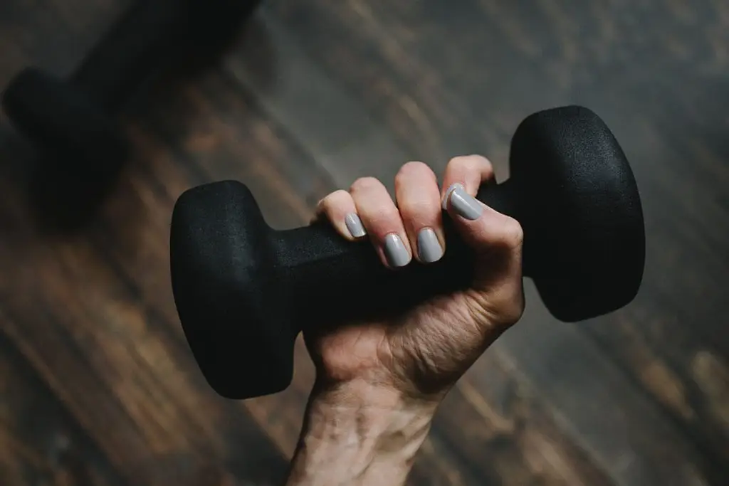Hombre con uñas pintadas sostiene una mancuerna negra en el gimnasio