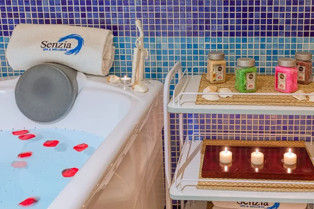 Tumbona spa con toallas, vela encendida y frascos arom&aacute;ticos junto a piscina.