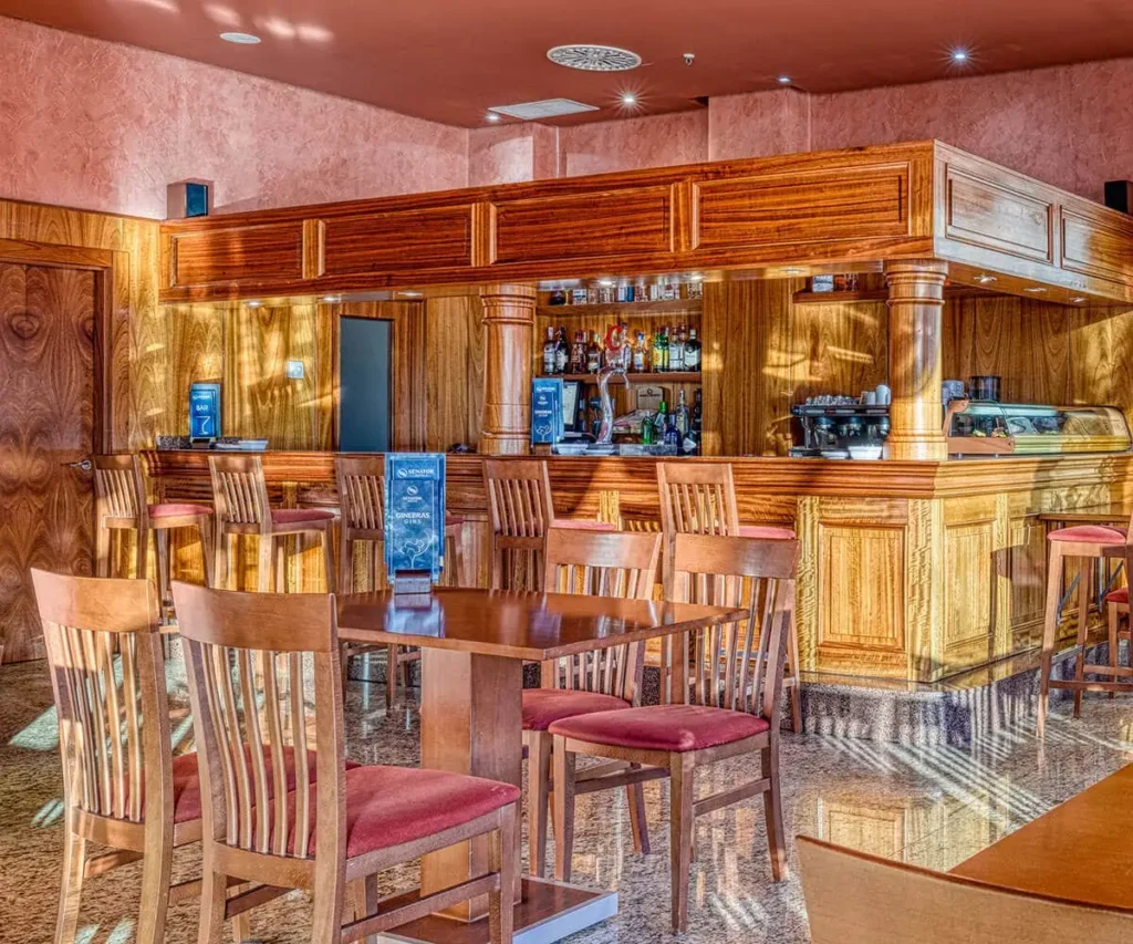 Bar con barra de madera, sillas, botellas y m&aacute;quinas de caf&eacute; en un ambiente c&aacute;lido