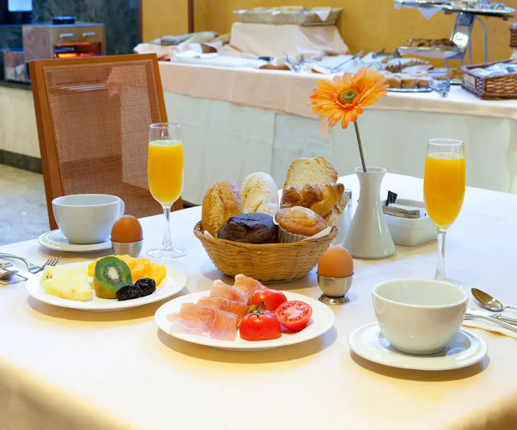 Mesa de desayuno con pan, huevos, frutas y dos copas de jugo naranja.