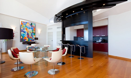 Sala moderna con suelo de madera, barra y sillas blancas, y arte colorido.