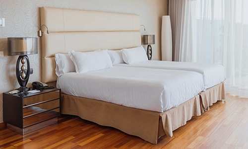 Habitaci&oacute;n moderna con dos camas, l&aacute;mparas y ventanal.