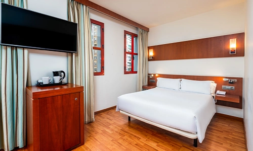 Habitaci&oacute;n de hotel moderna con cama, televisor y cafetera.