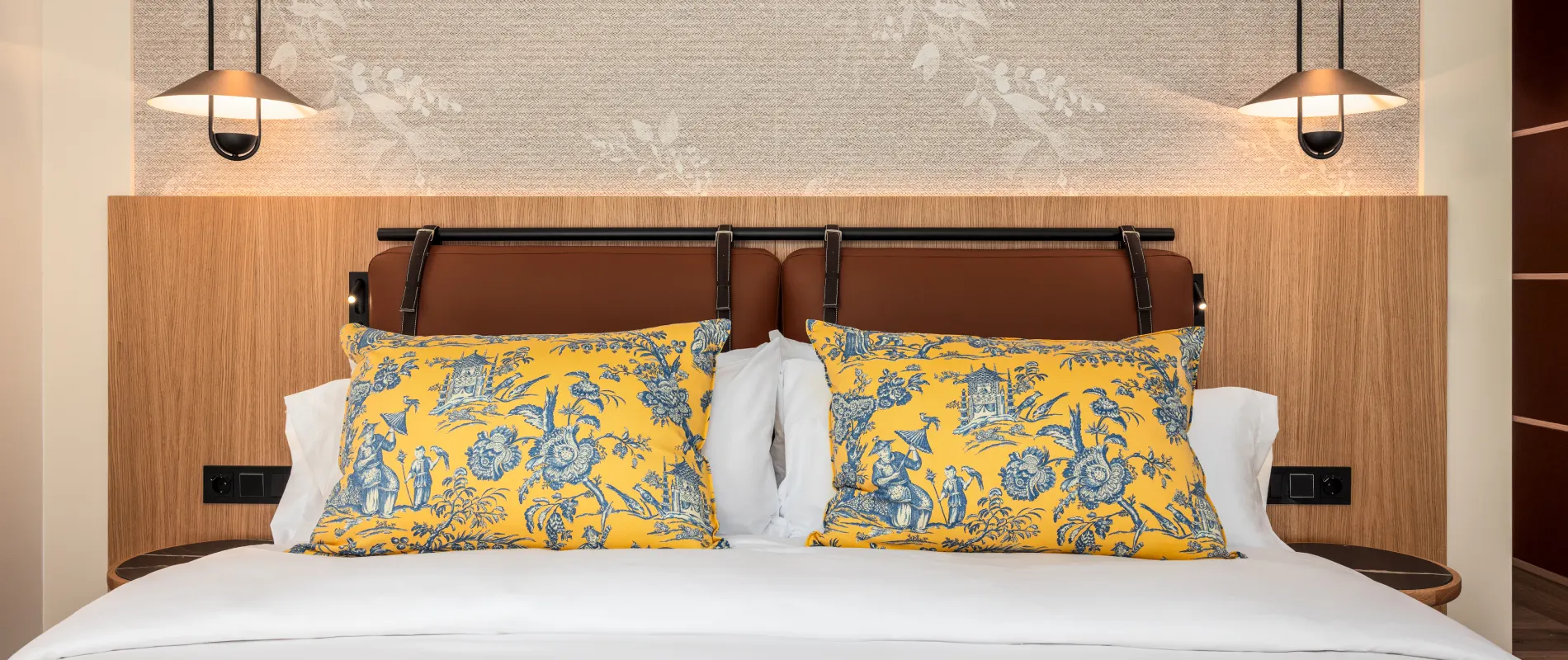 Habitaci&oacute;n de hotel con cama blanca y cojines amarillos con estampado azul, luz arriba
