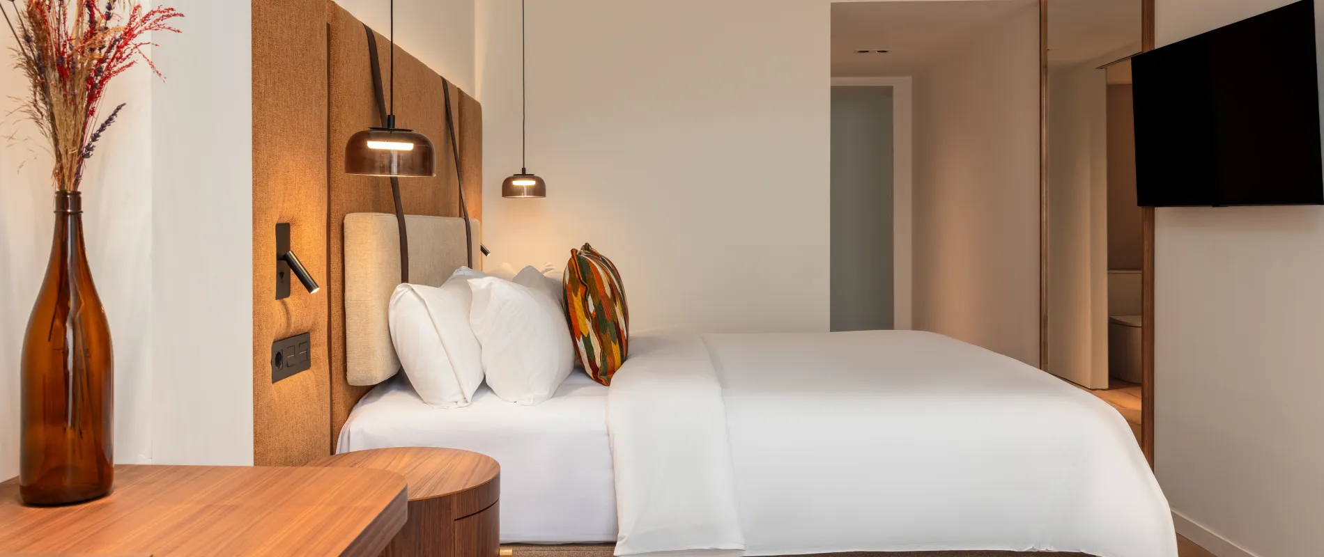 Dormitorio moderno con cama blanca, l&aacute;mparas colgantes y paneles de madera