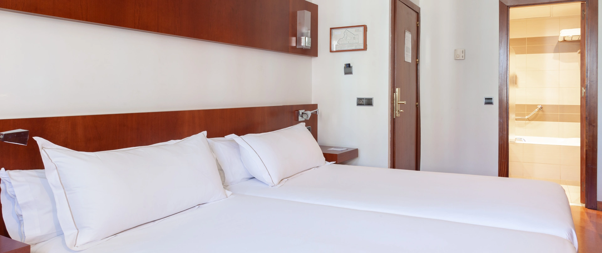 Dormitorio con cama de s&aacute;banas blancas y puerta al ba&ntilde;o con ducha