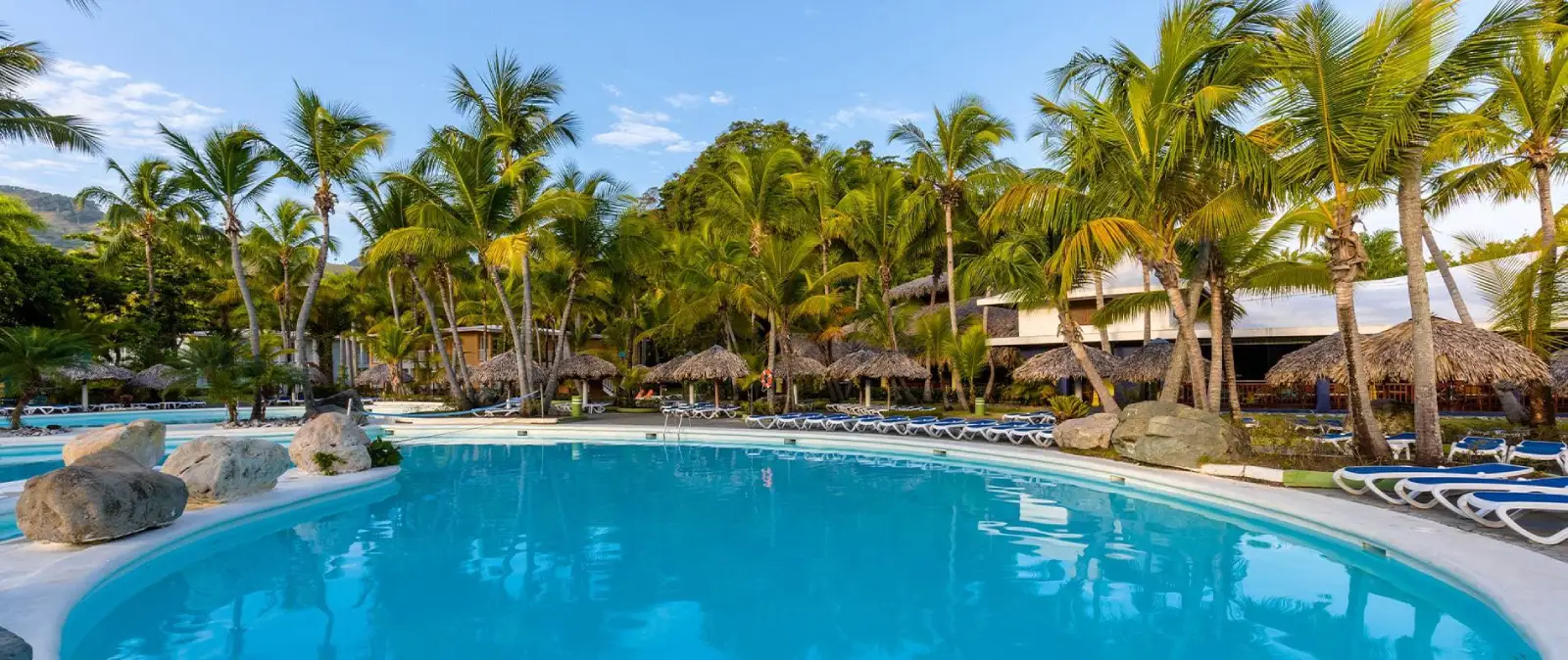 Piscina tropical con palmeras y tumbonas en un resort, cielo azul