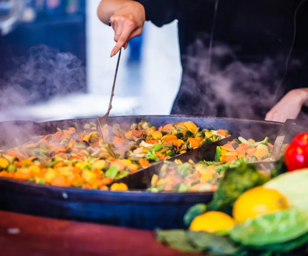 Cocinero revuelve verduras en una sart&eacute;n humeante con una cuchara.