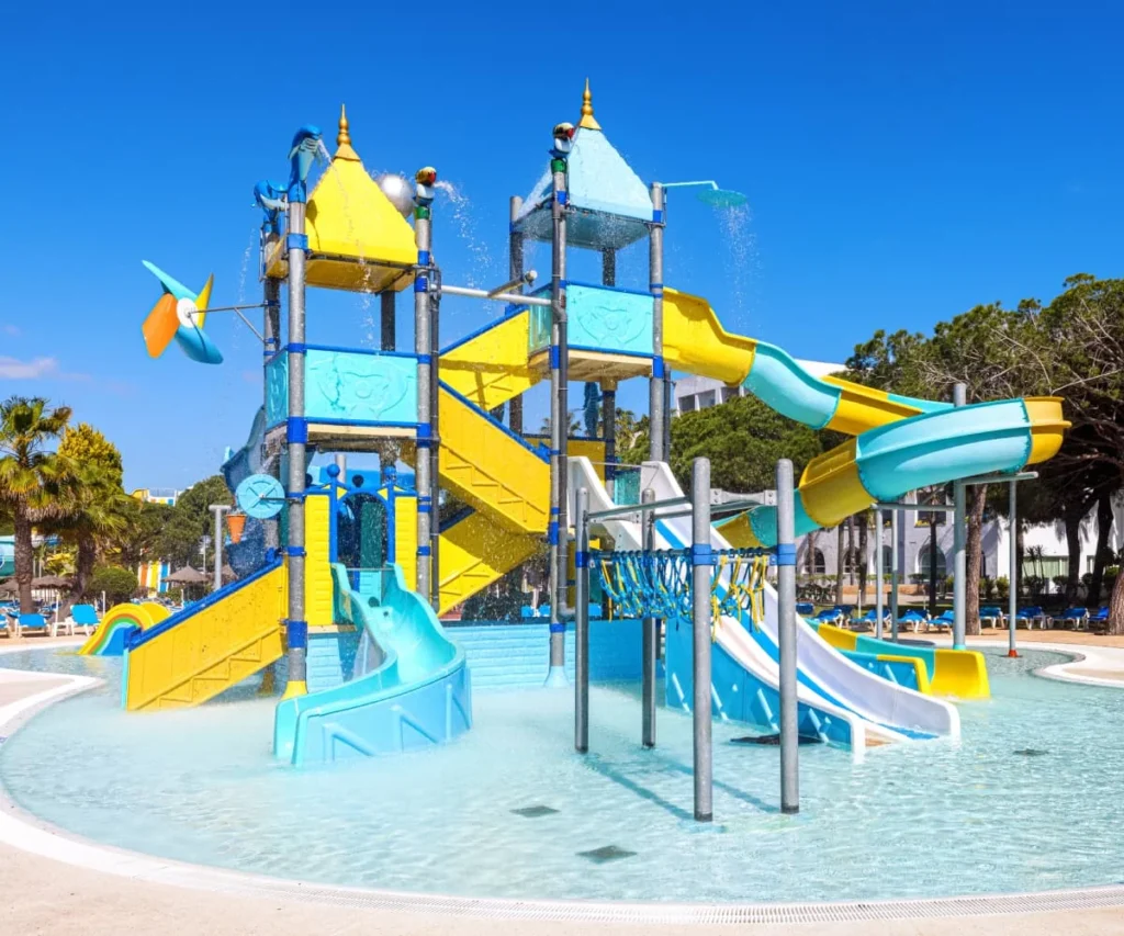 Parque acu&aacute;tico con toboganes de colores y fuente de agua en piscina al sol