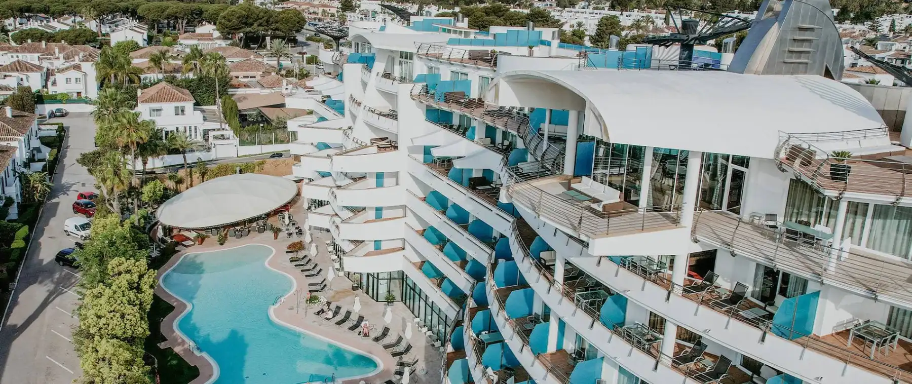 Vista a&eacute;rea de un hotel con piscina, edificios blancos y terrazas azules.