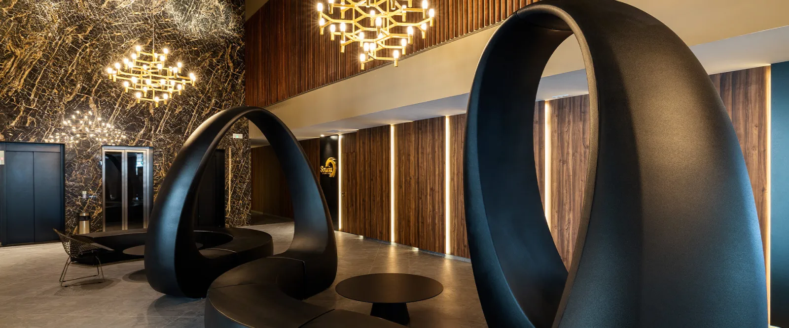 Lobby moderno con esculturas ovaladas negras, m&aacute;rmol y luces colgantes.