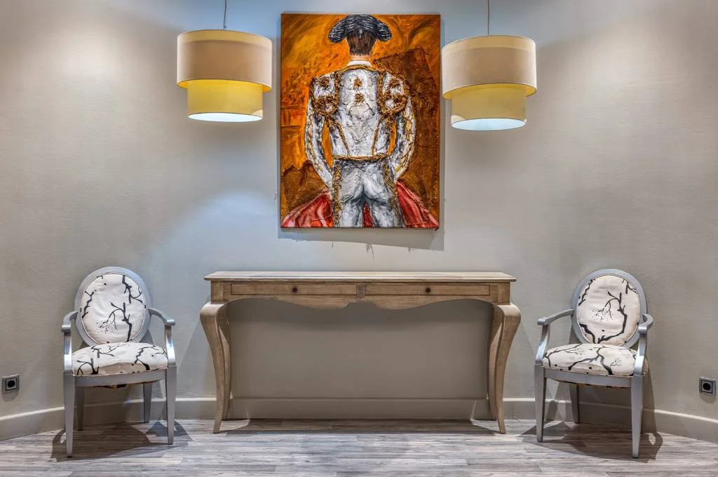 Sala con dos sillones, consola de madera y cuadro de un &aacute;ngel bajo l&aacute;mparas
