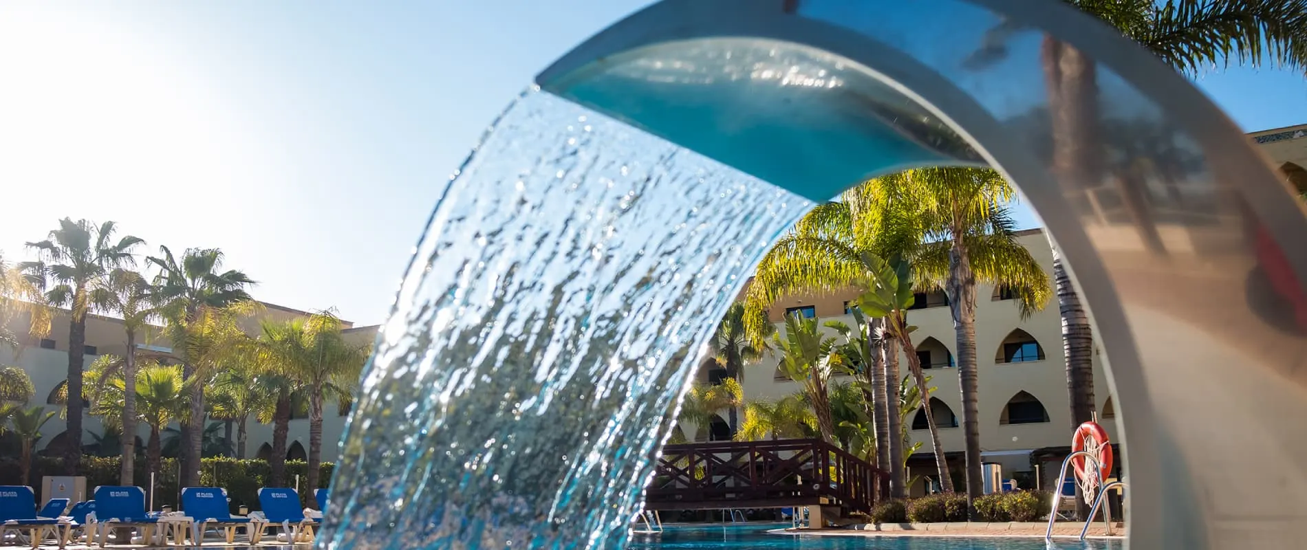 C&uacute;pula de cristal con agua, palmeras y piscina en un hotel al sol.