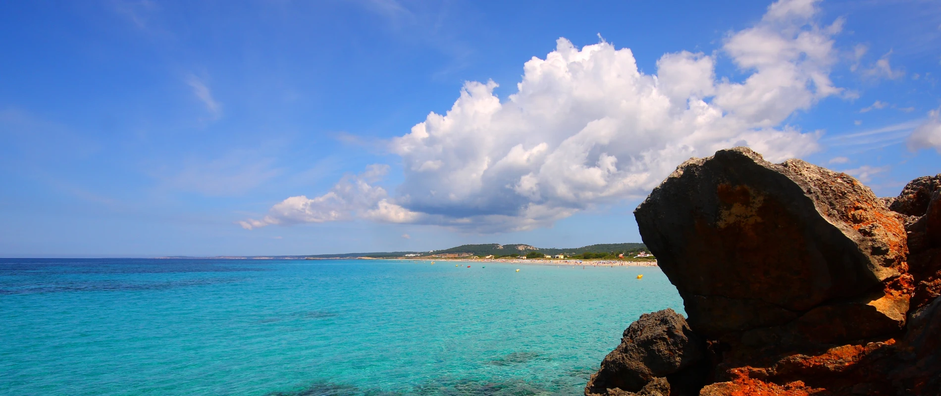 Mar turquesa y una roca costera con cielo azul y nubes blancas