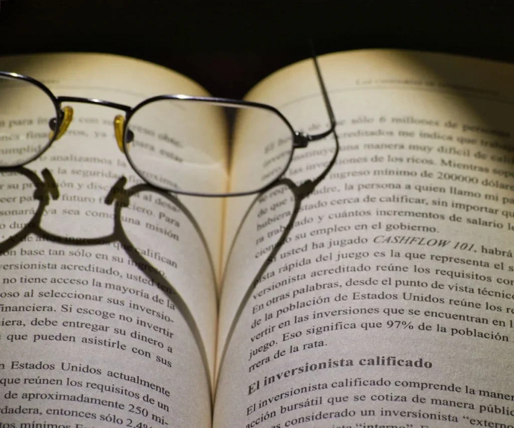 Gafas sobre un libro abierto con texto legible al fondo.