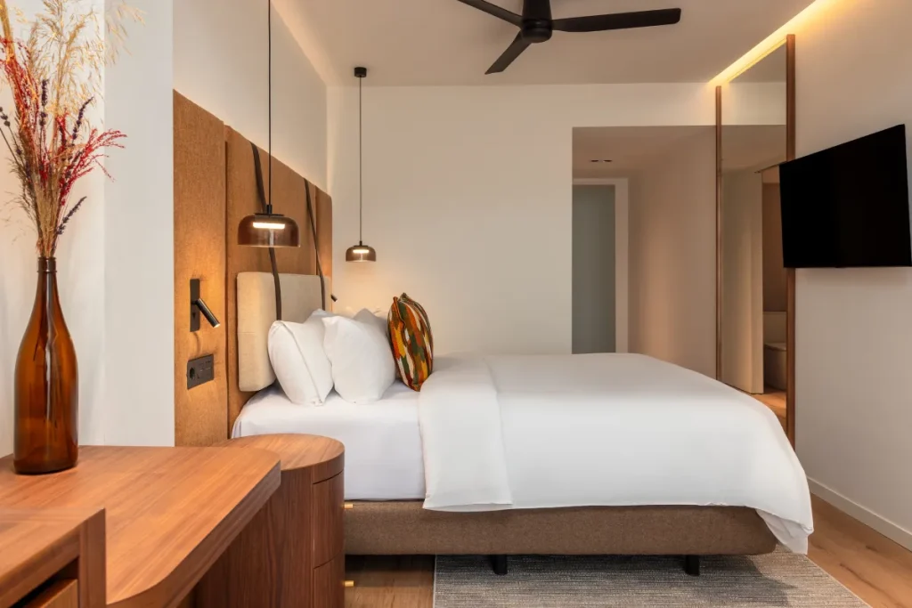 Dormitorio moderno con cama blanca, l&aacute;mparas colgantes y TV de pared