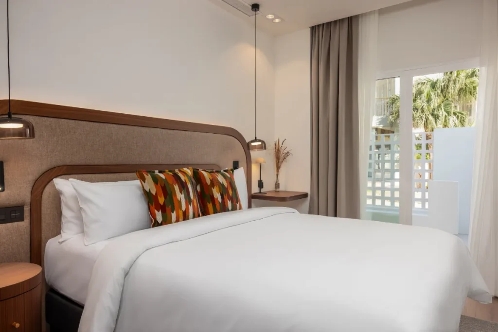 Dormitorio moderno con cama, coj&iacute;n estampado y cortinas frente a ventana.