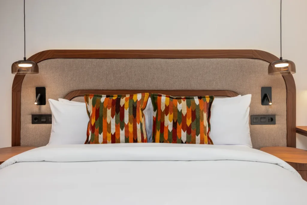 Dormitorio con cama tapizada, cojines blancos y almohadones con patr&oacute;n multicolor