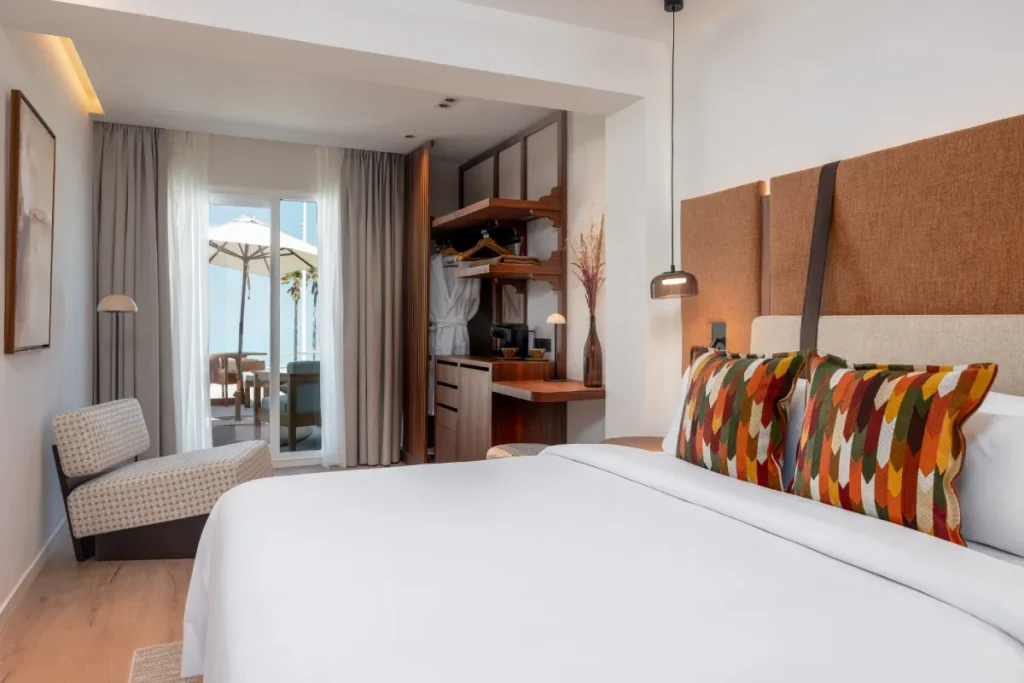 Dormitorio moderno con cama blanca, cojines coloridos y ventana al balc&oacute;n