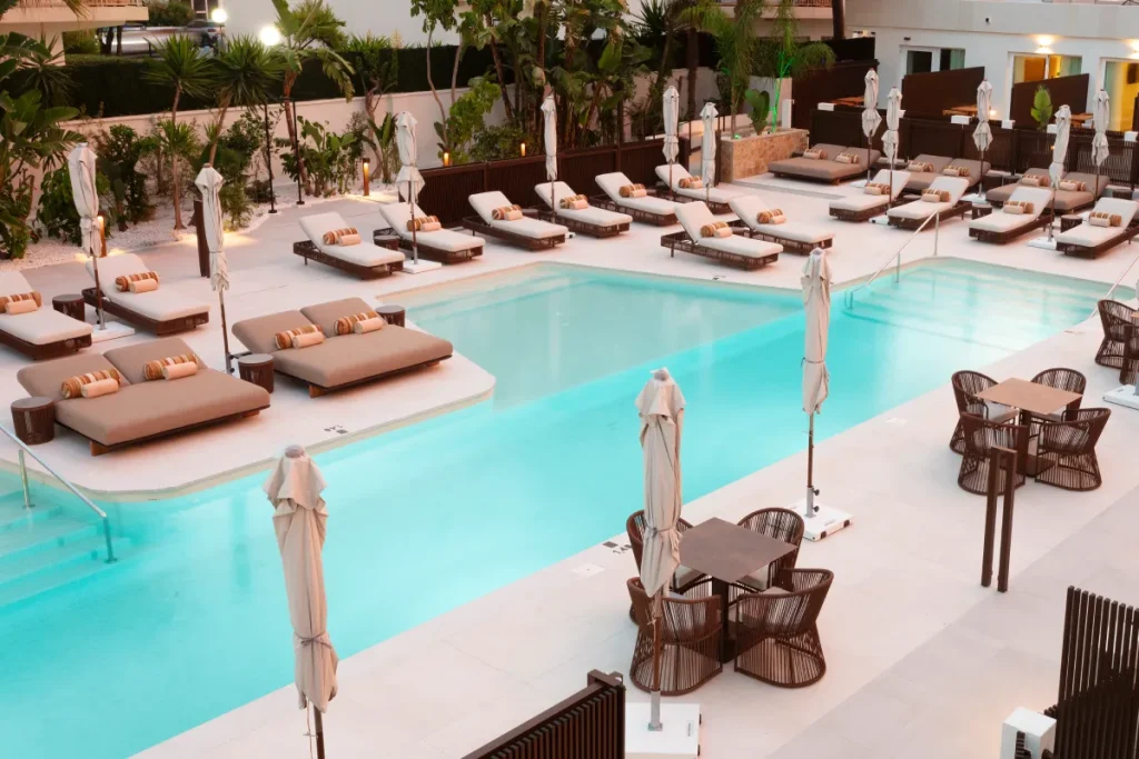Piscina al aire libre con tumbonas y sombrillas, rodeada de palmeras y luces
