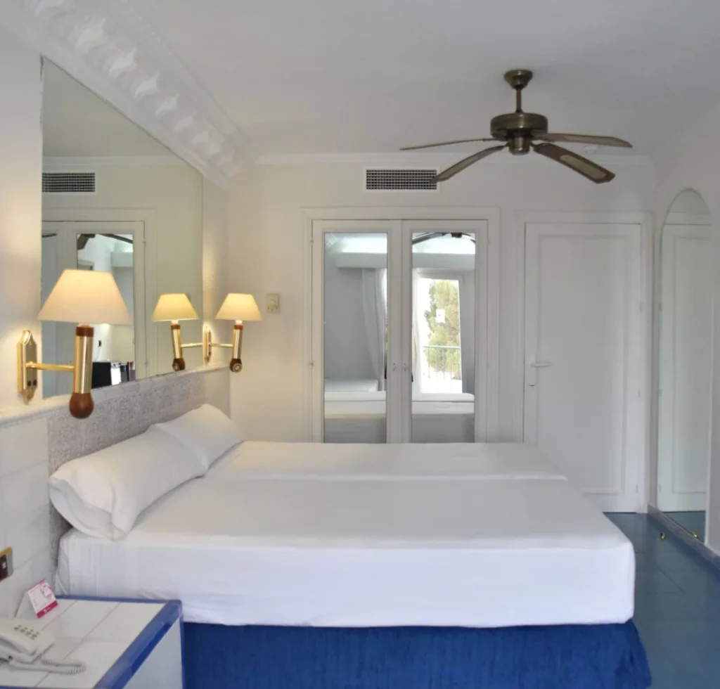 Dormitorio moderno con cama blanca, l&aacute;mparas y ventilador de techo.