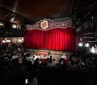 Escenario con cortina roja y audiencia en un teatro.