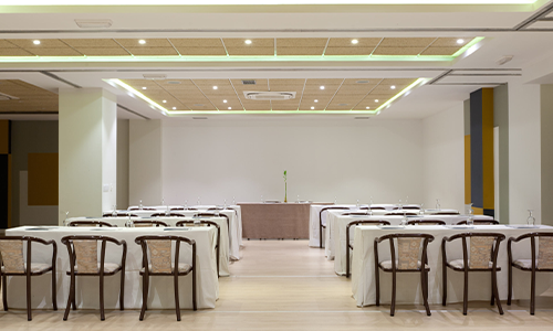 Sala de conferencias vac&iacute;a con sillas y mesas blancas.